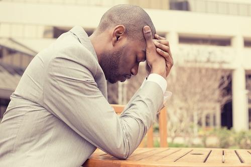 Side profile stressed young businessman sitting outside corporate office