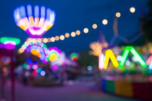 Blurred image of people in funfair amusement park festival in city park at night bokeh background. Summer festival holiday vacation concept.